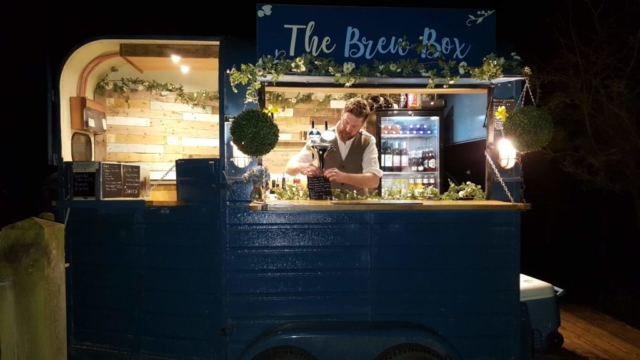 The Brew Box lit up at night, with a barman inside